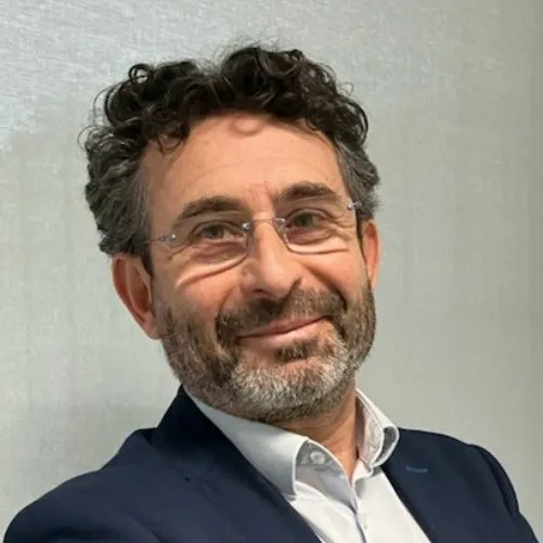 Portrait de Laurent Casartelli avec une veste de costume bleue, une chemise et des lunettes, la tête légèrement penchée vers la droite