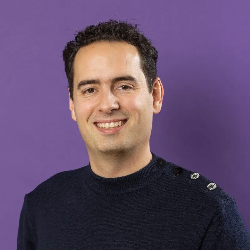 Portrait de Valentin Rabanelly sur fond violet, avec un pull bleu foncé et 2 boutons sur l'épaule gauche